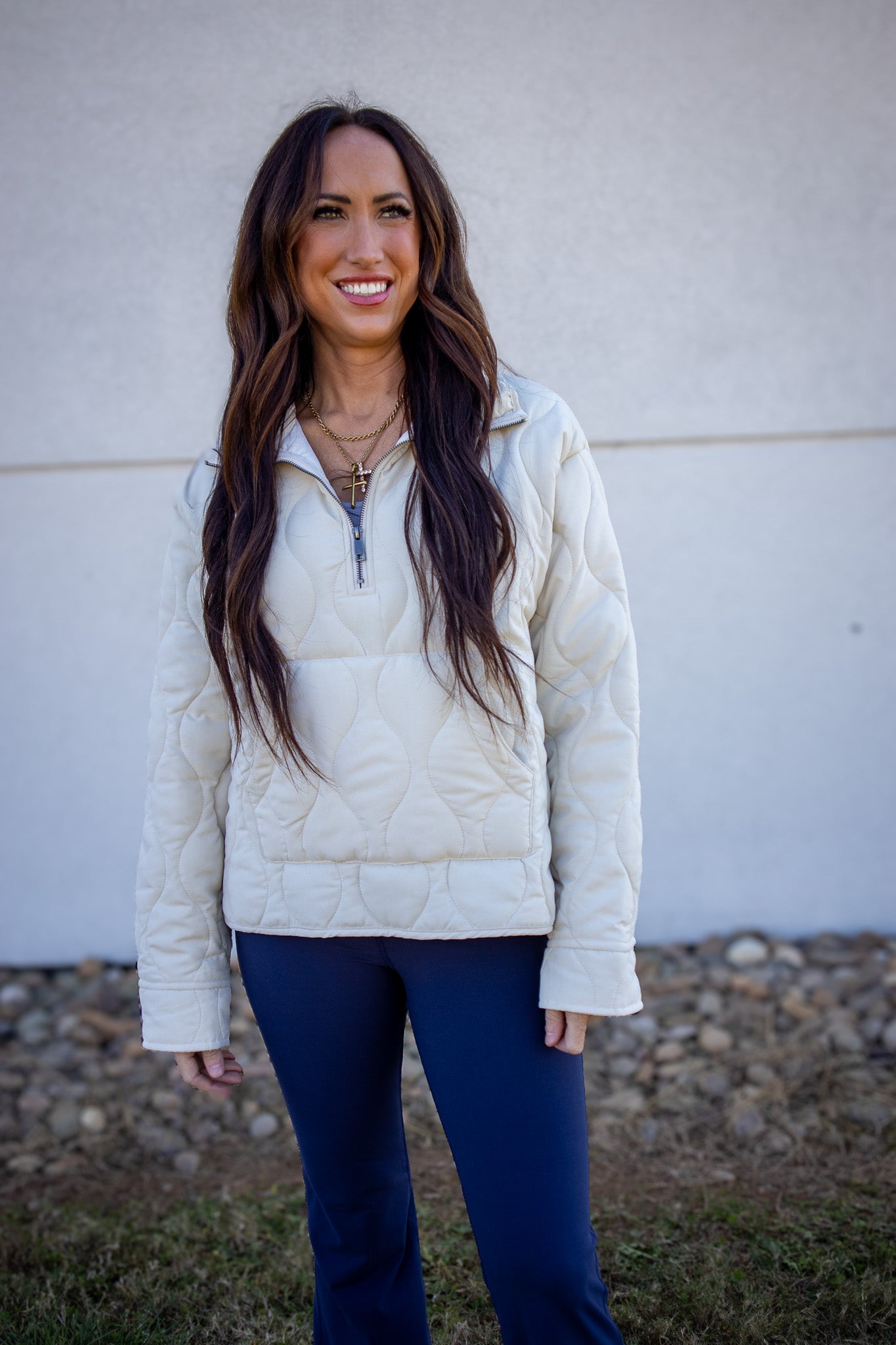 Woman wearing a white quilted jacket and blue pants standing against a plain background