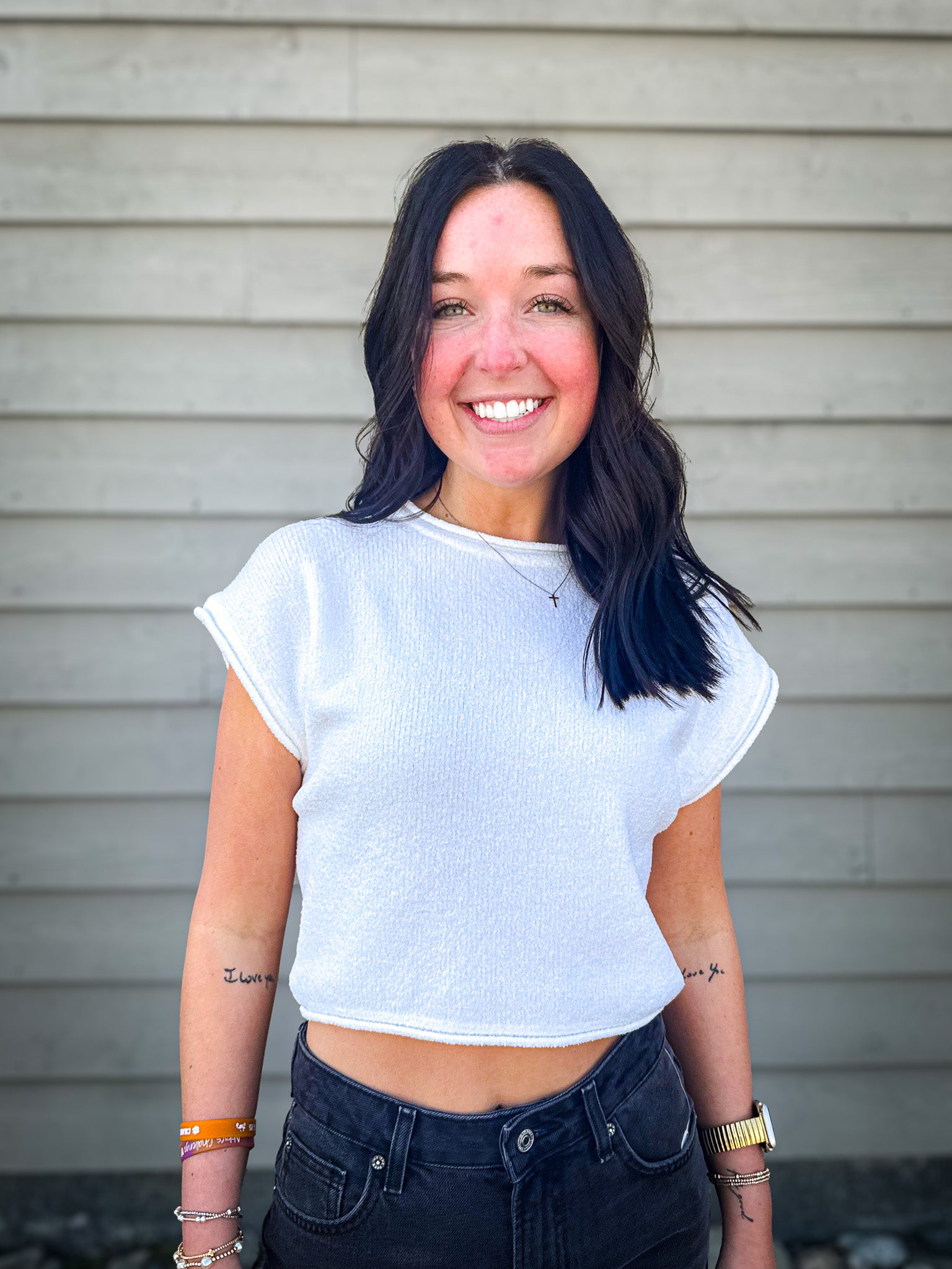 Woman wearing a white crop top and dark jeans standing against a neutral background