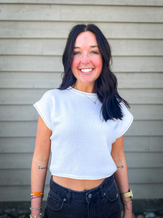 Woman wearing a white crop top and dark jeans standing against a neutral background
