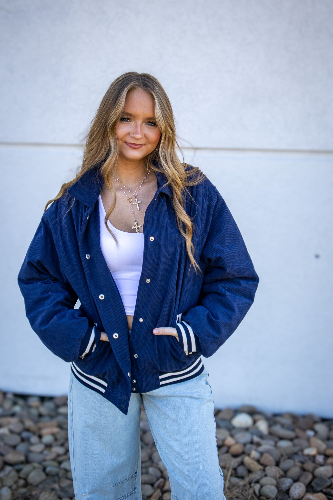 Woman wearing a blue jacket with white trim against a white wall.