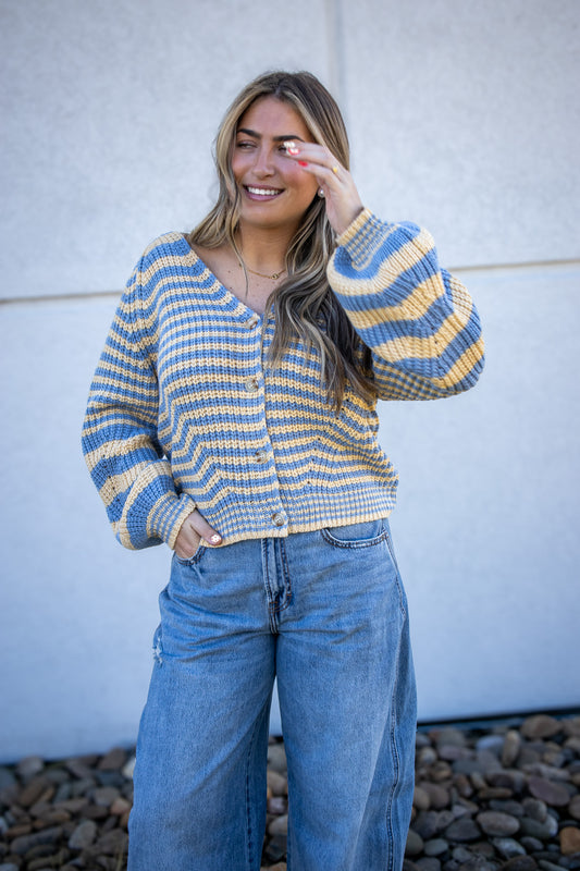 Woman wearing a striped sweater and jeans standing against a light-colored wall.