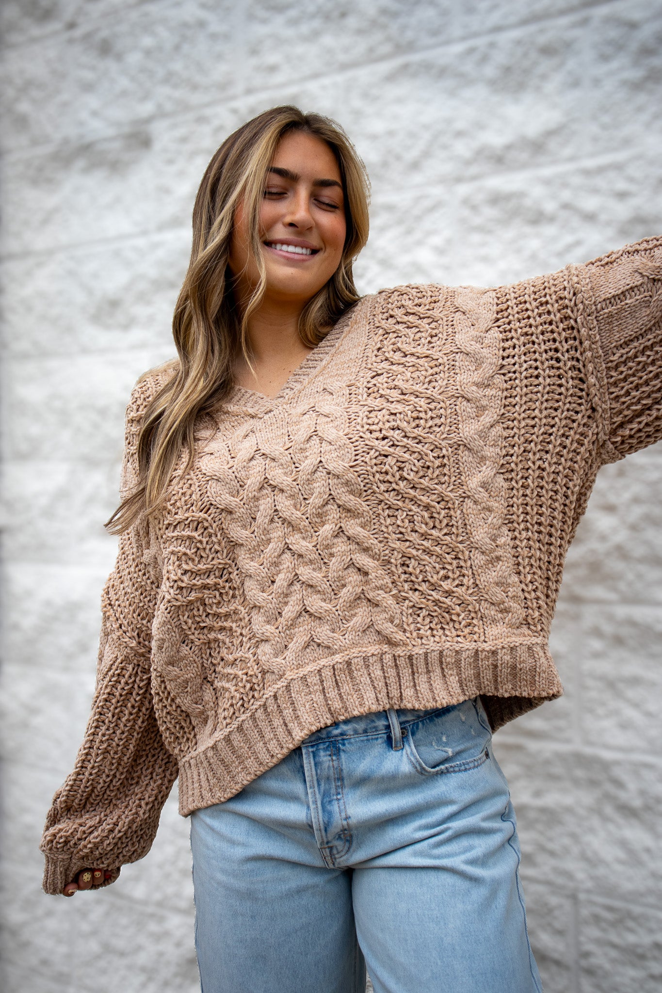 Woman wearing a beige chunky knit sweater and light blue jeans against a neutral background