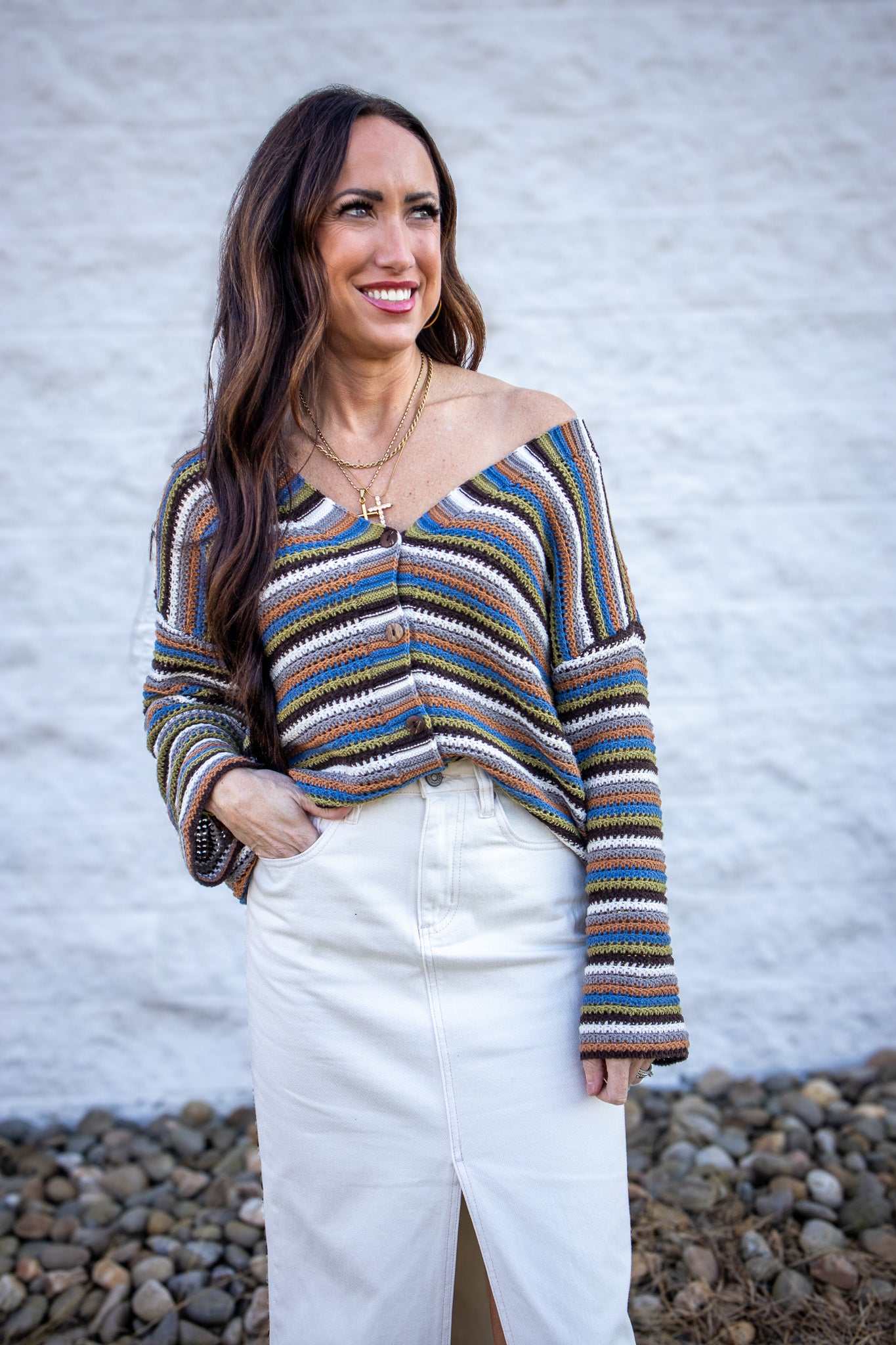 Woman wearing a colorful striped sweater and white pants against a textured wall.