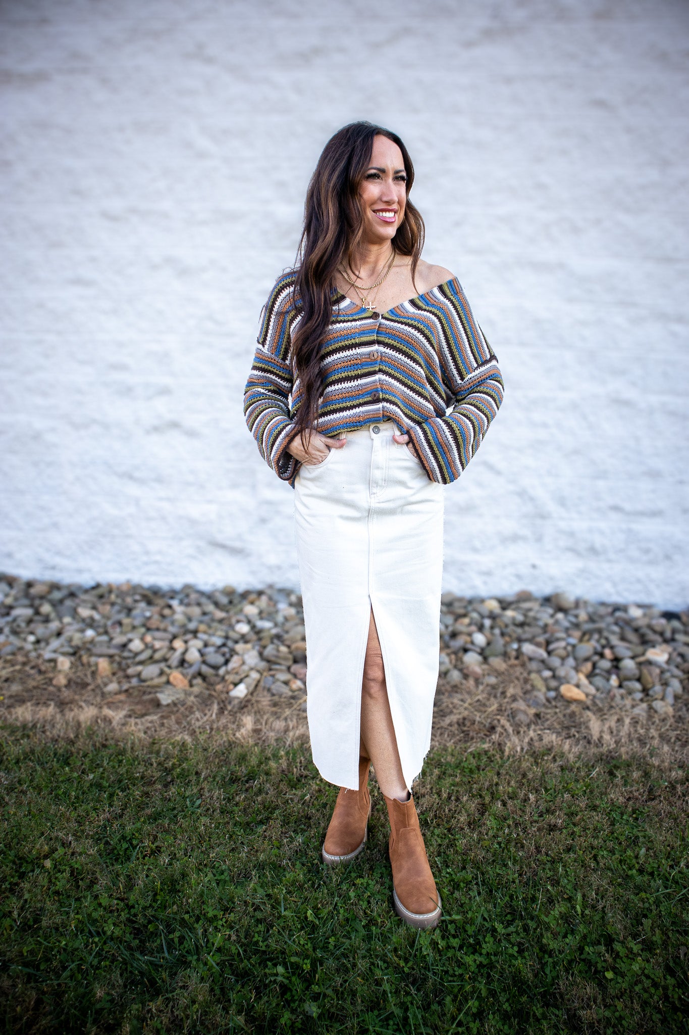 Woman wearing a striped sweater and white skirt standing in front of a white wall.