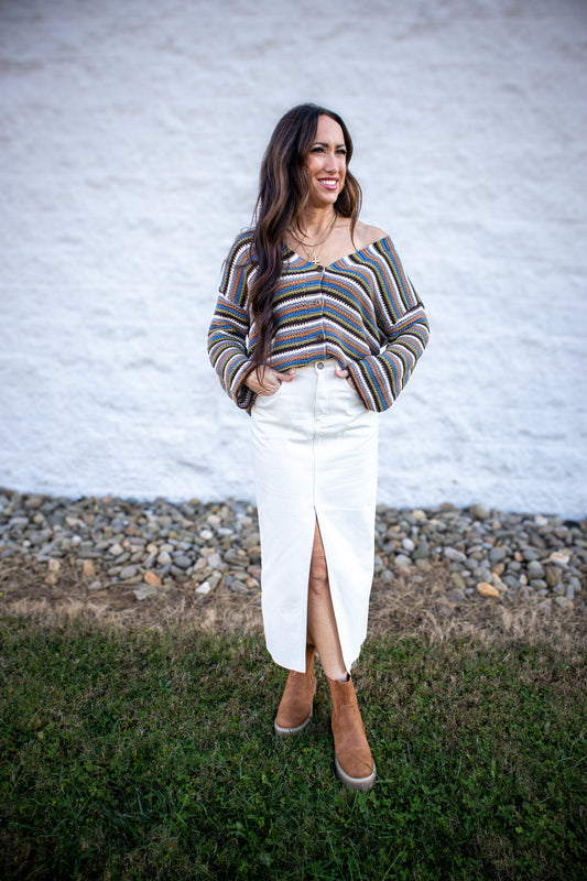 Woman wearing a striped sweater and white skirt standing in front of a white wall.