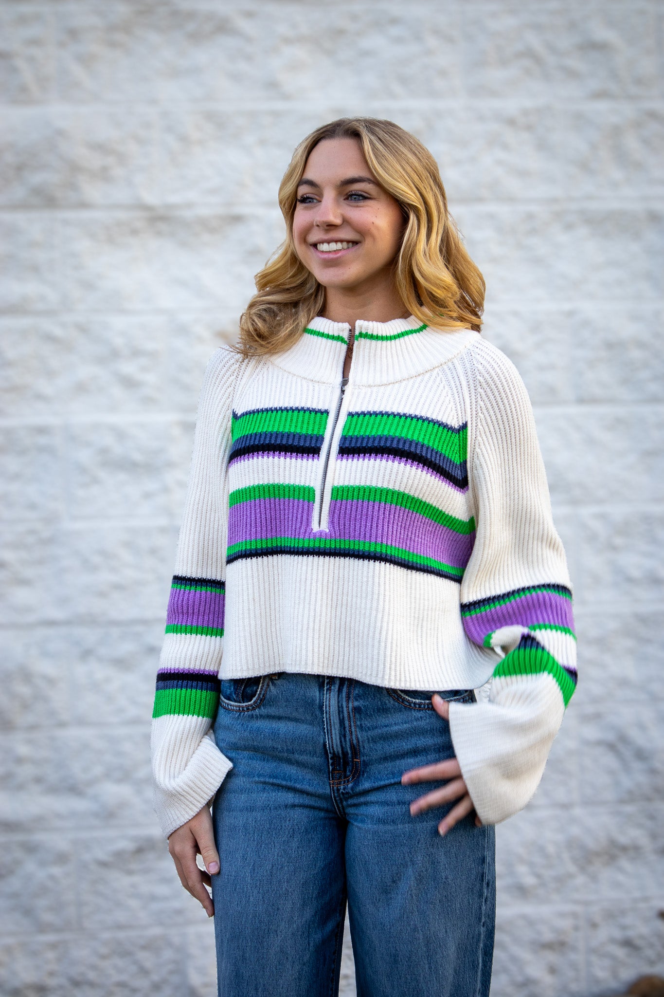 Woman wearing a white sweater with colorful stripes against a gray wall