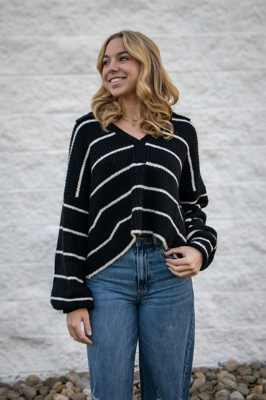 Woman wearing a black and white striped sweater and blue jeans against a gray wall.