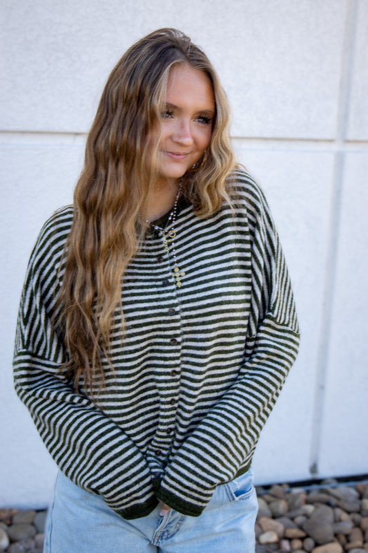 Woman wearing a striped shirt standing against a light-colored wall.