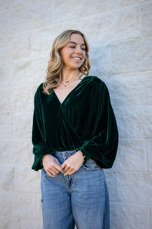 Woman wearing a green velvet top and blue jeans against a textured wall.
