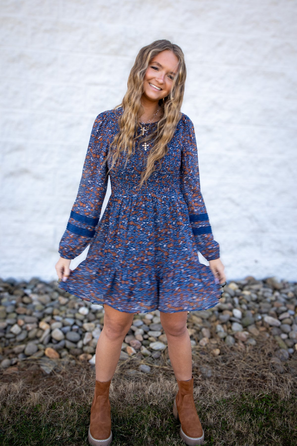 Woman wearing a blue floral dress standing outdoors against a white wall.