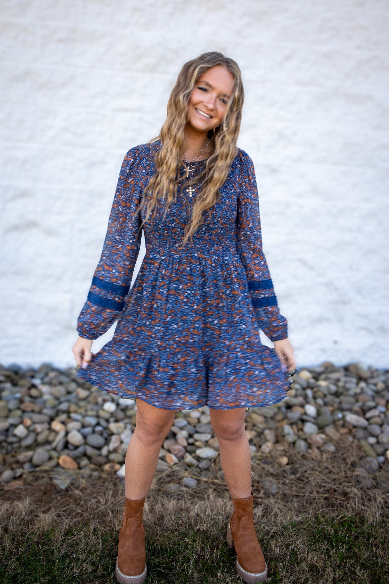 Woman wearing a blue floral dress standing outdoors against a white wall.