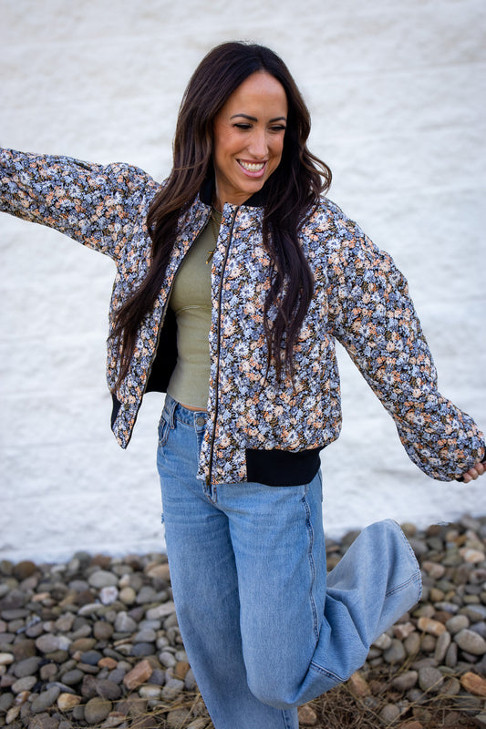 Woman wearing a floral jacket and jeans against a white wall.