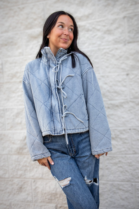 Person wearing a denim jacket and jeans against a textured wall.