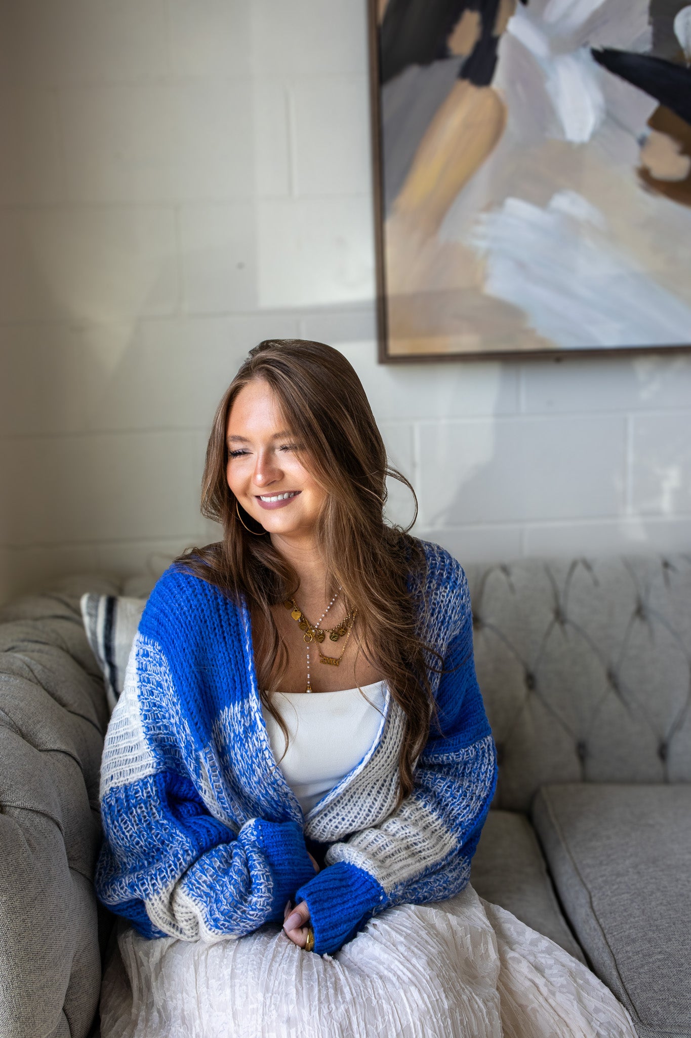Woman wearing a blue and gray cardigan sitting on a couch in a living room.