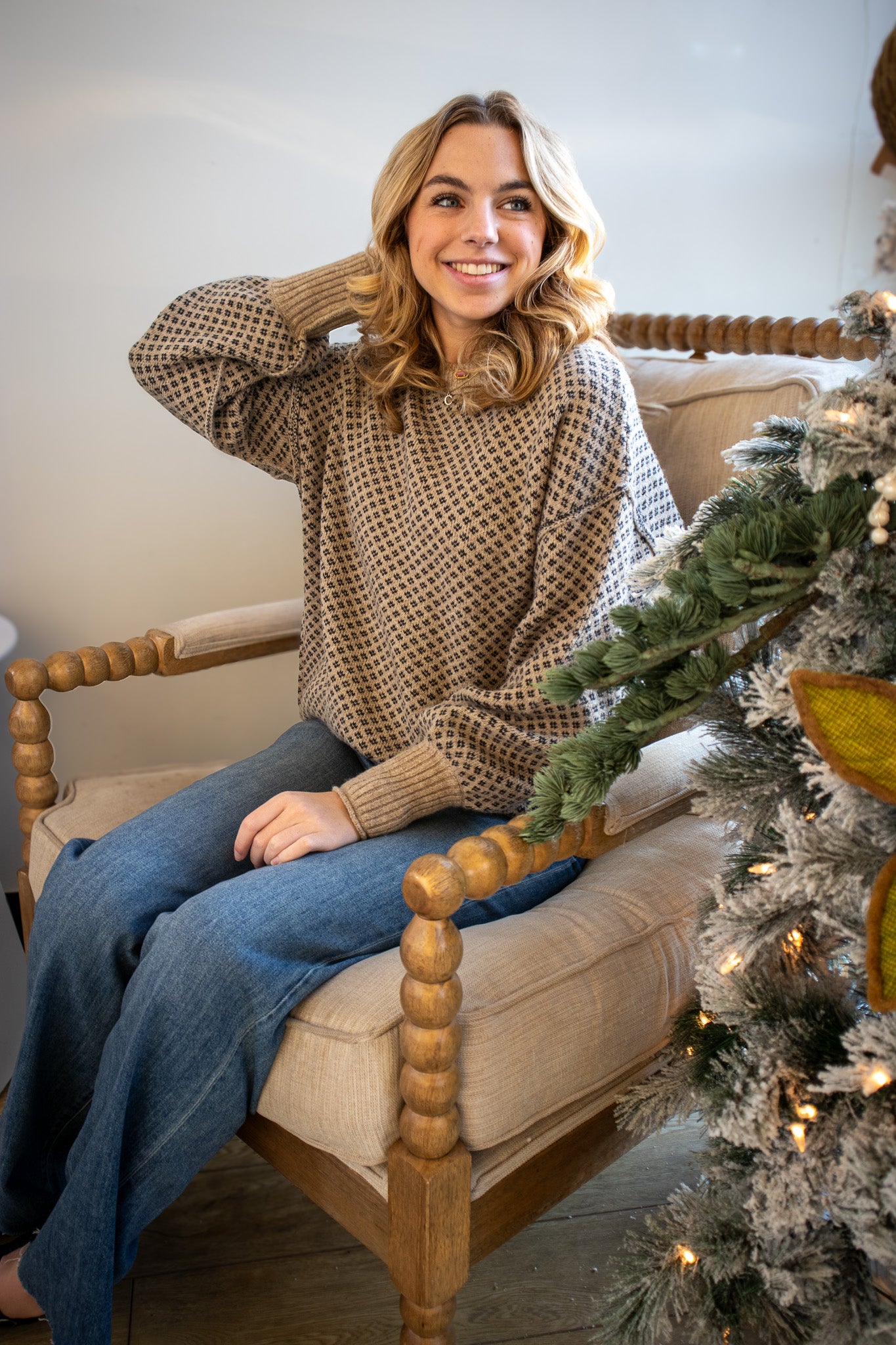 Woman sitting on a wooden chair next to a decorated Christmas tree