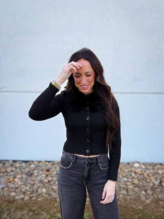 Woman wearing a black ribbed sweater with a removable fur collar. 