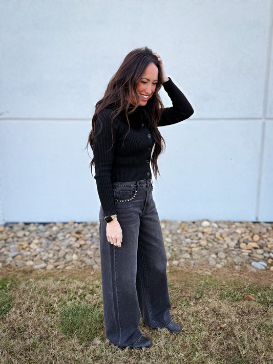 Woman wearing a black top and black wide leg jeans with studded detail