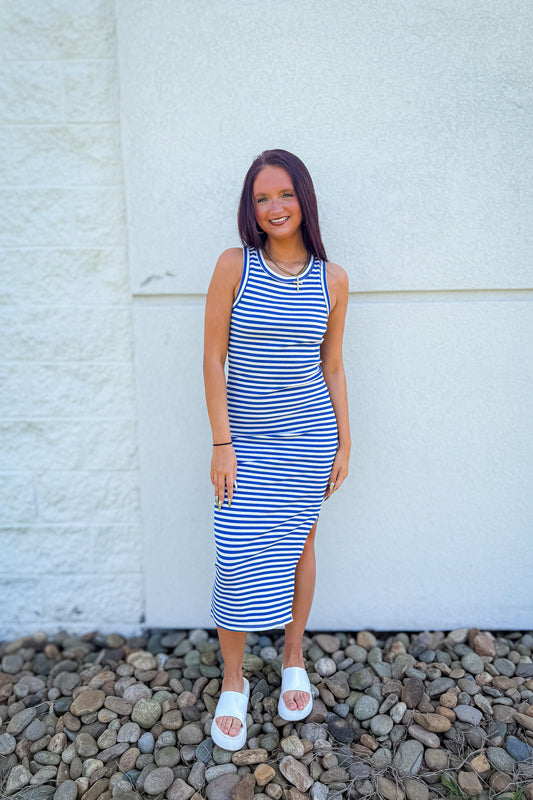 Model wearing a blue and white striped midi dress with a side slit, styled with white slide sandals for an easy summer boutique outfit perfect for vacation, beach days, and casual weekend wear.