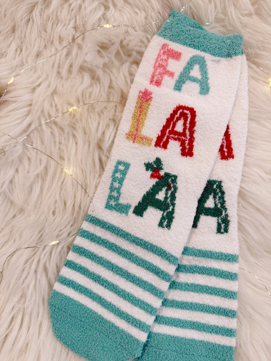 Christmas-themed socks with 'FA LALA' text on a fluffy white surface.