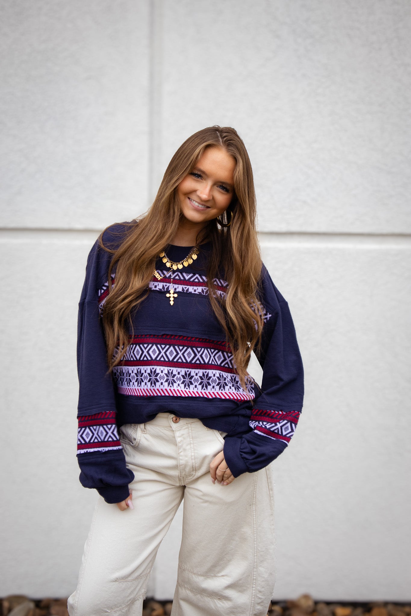 Woman wearing a patterned sweater and white pants against a plain background