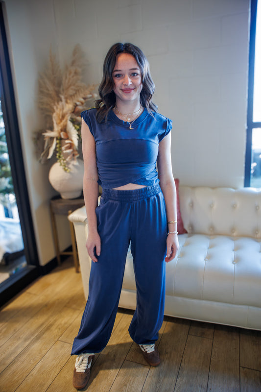 Woman in a blue outfit standing in a room with a white couch and decorative items.