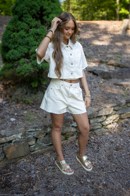 Woman in a white outfit standing outdoors with greenery in the background