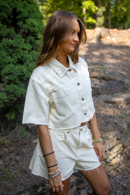 Woman wearing a white denim outfit standing outdoors with greenery in the background
