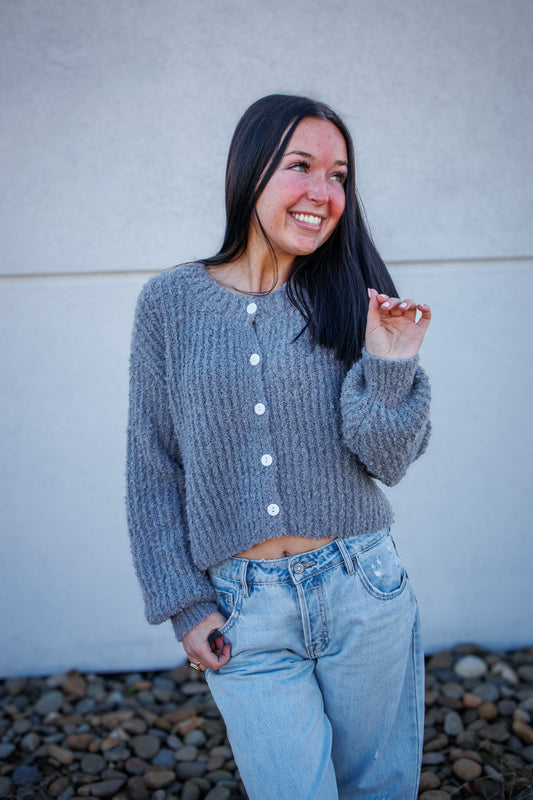 Woman wearing a gray knitted cardigan and light blue jeans against a plain background