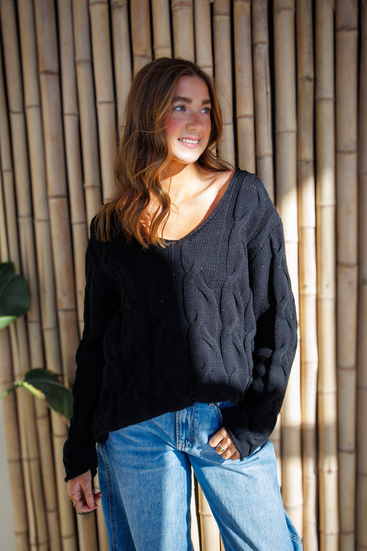 Woman wearing a black sweater and blue jeans standing against a bamboo wall.
