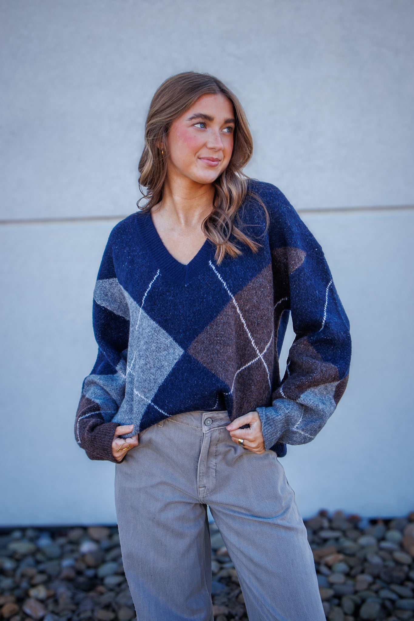 Woman wearing a blue and brown patterned sweater against a gray wall.
