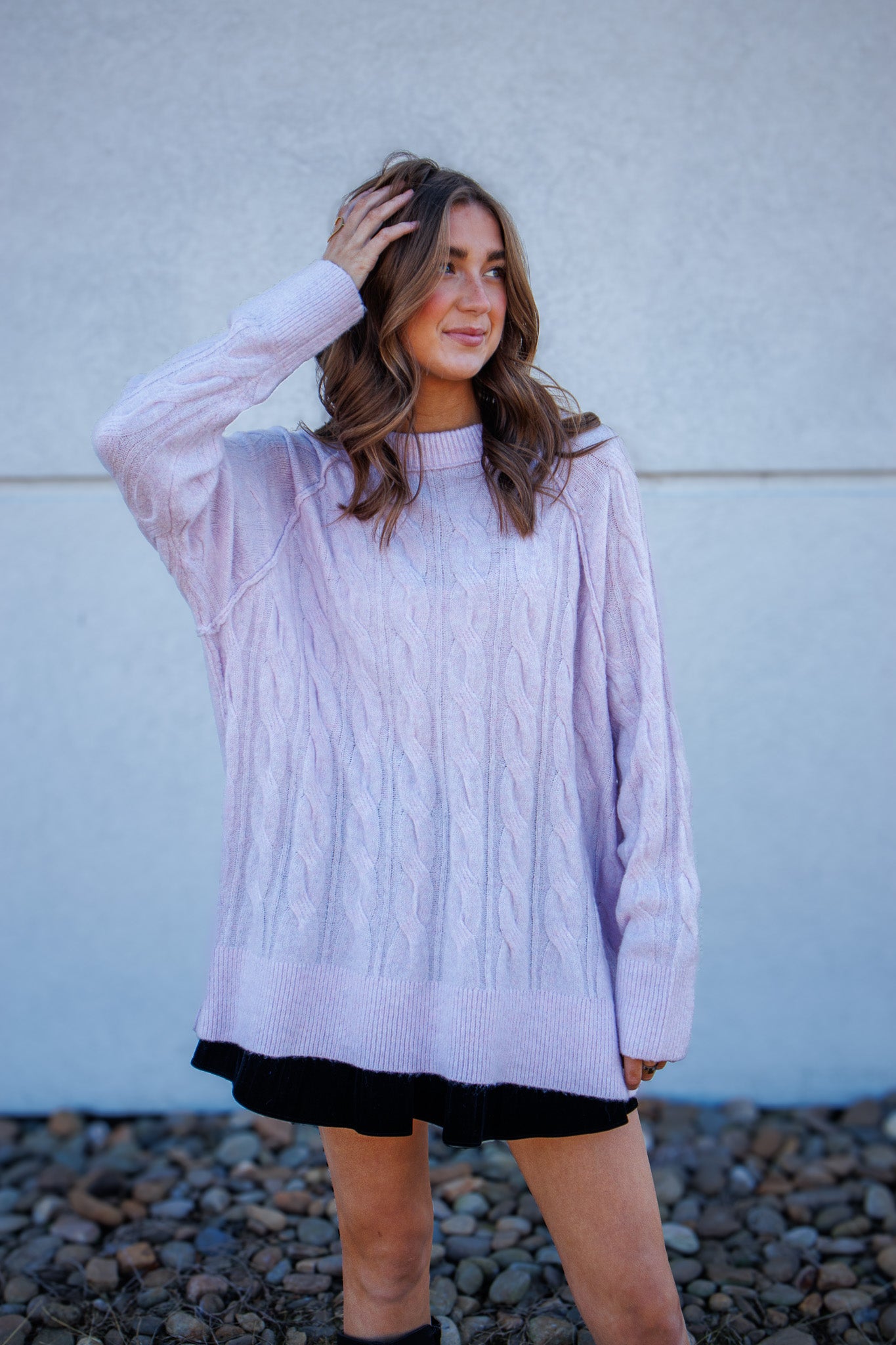 Woman wearing a light purple sweater over a black dress against a plain background