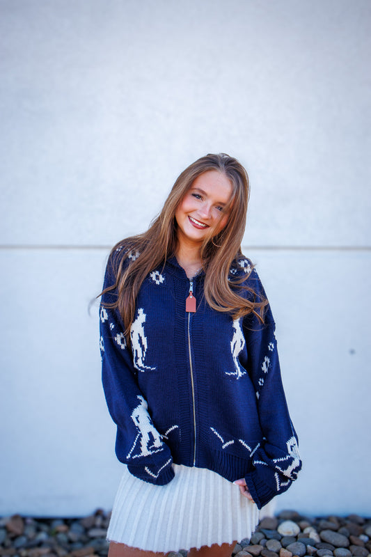 Woman wearing a navy blue cardigan with white patterns against a white wall.