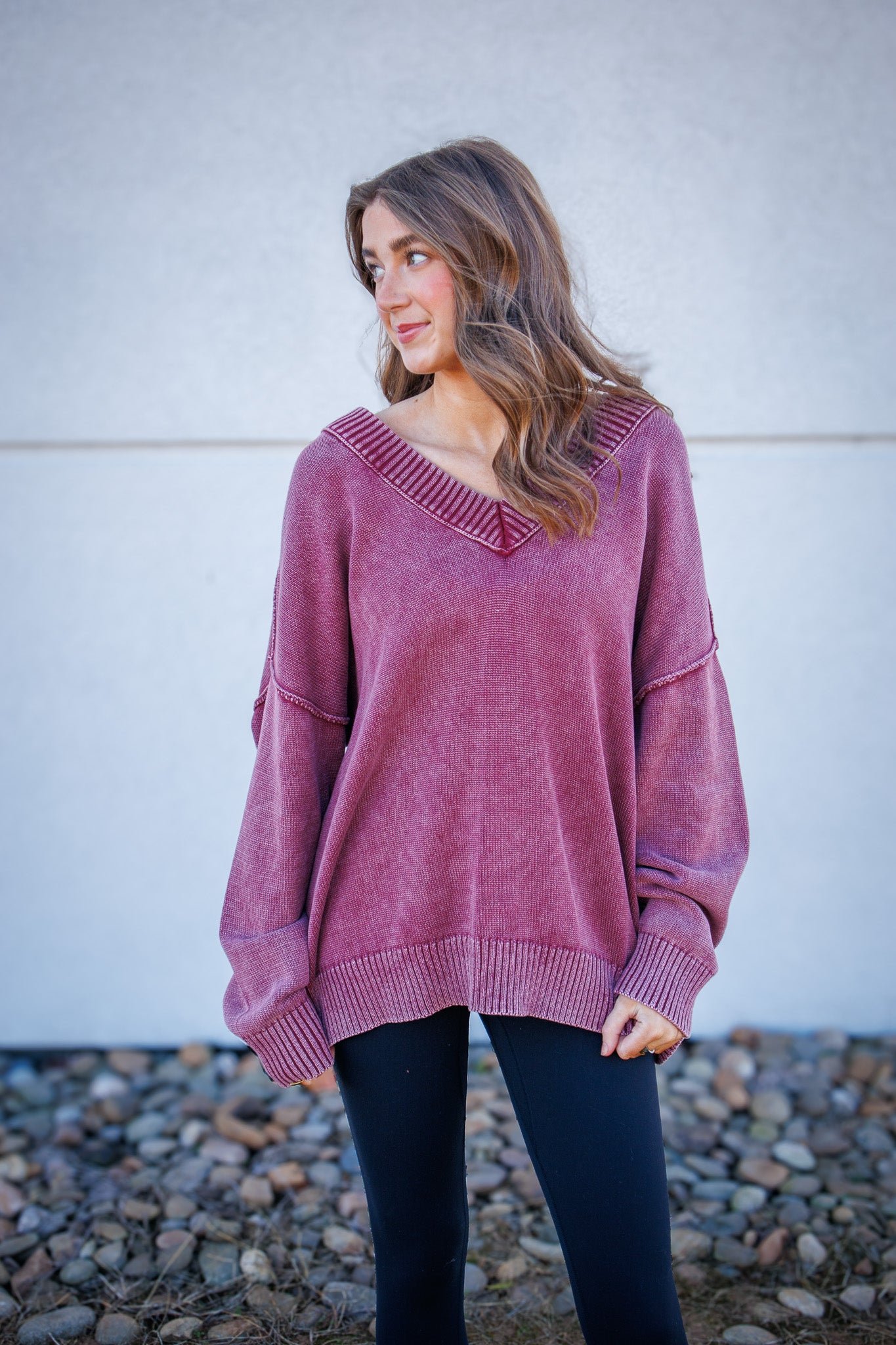 Woman wearing a red sweater standing against a white wall with a stone ground.