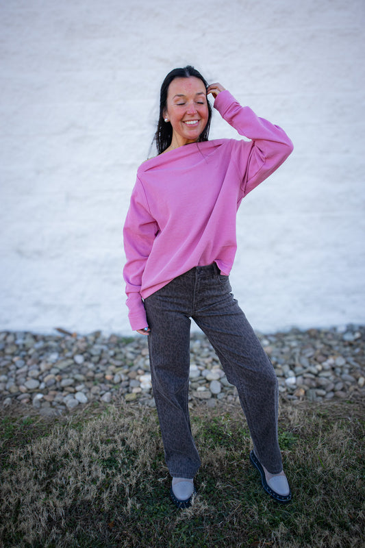 Person wearing a pink sweater and gray pants standing outdoors against a white wall.