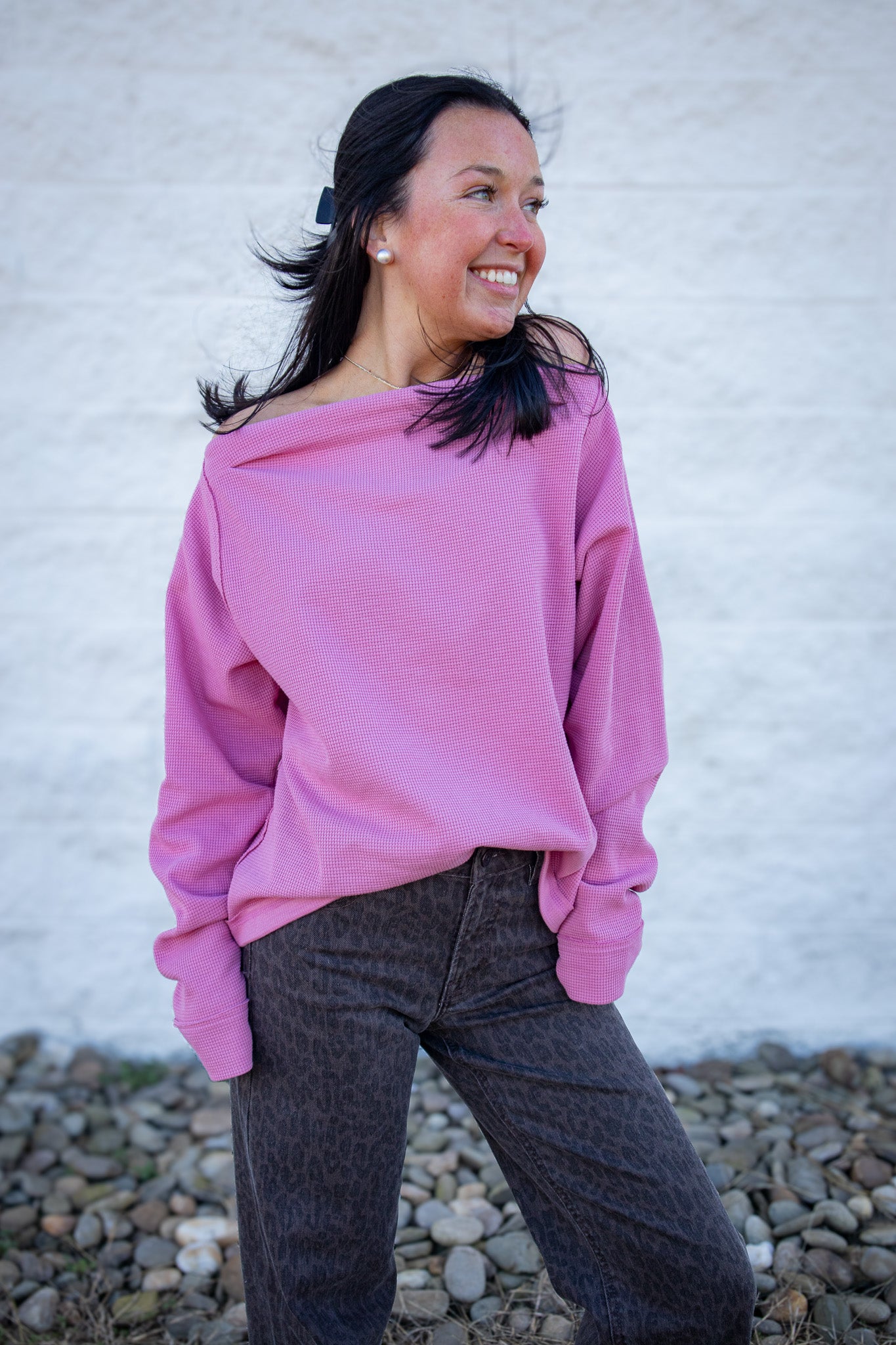 Woman wearing a pink sweater and dark pants against a white wall.