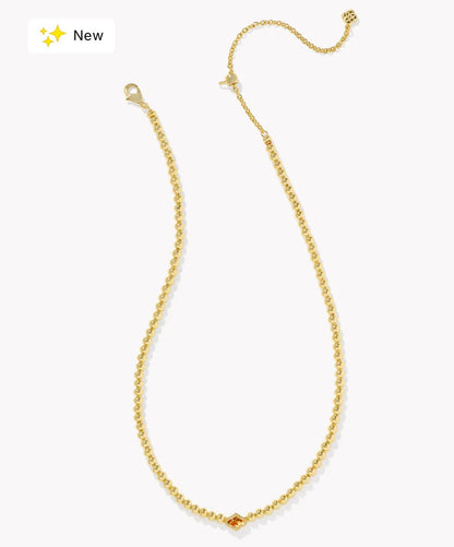 A delicate gold chain necklace with a small central gold bead and a tiny orange gemstone accent, displayed on a clean white background with a 'New' badge in the top-left corner.