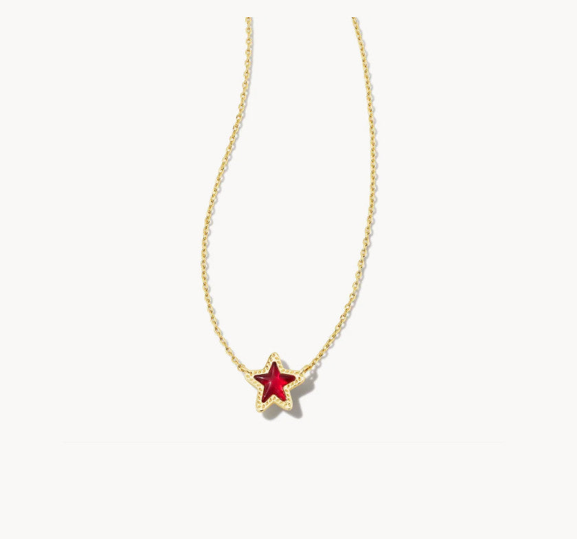 A delicate gold chain necklace featuring a small five-pointed star pendant with a vibrant red center and a gold border, set against a plain off-white background.