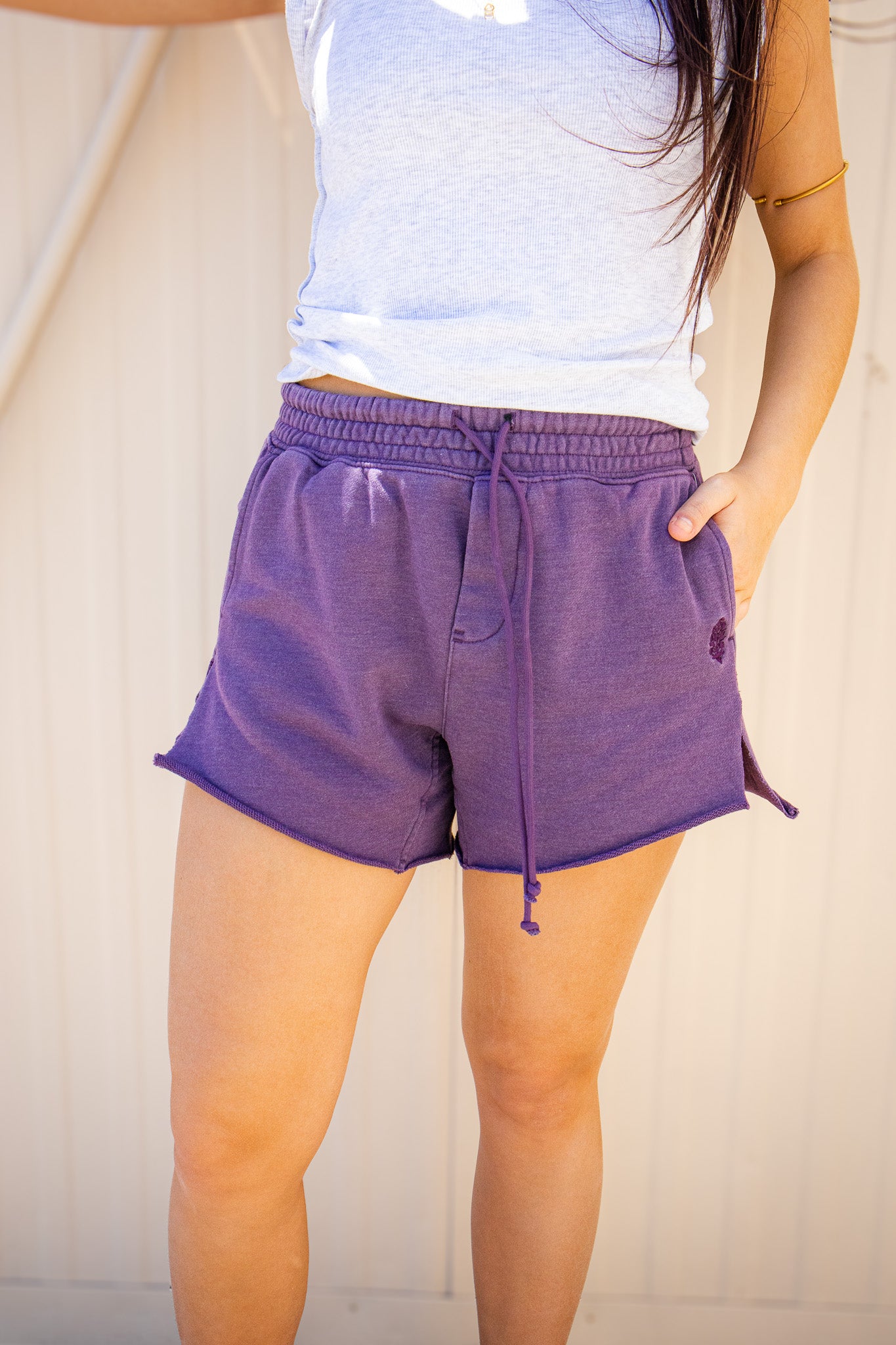 Purple Free People drawstring lounge shorts with an elastic waistband, side pockets, and raw hem styled with a white summer tank.
