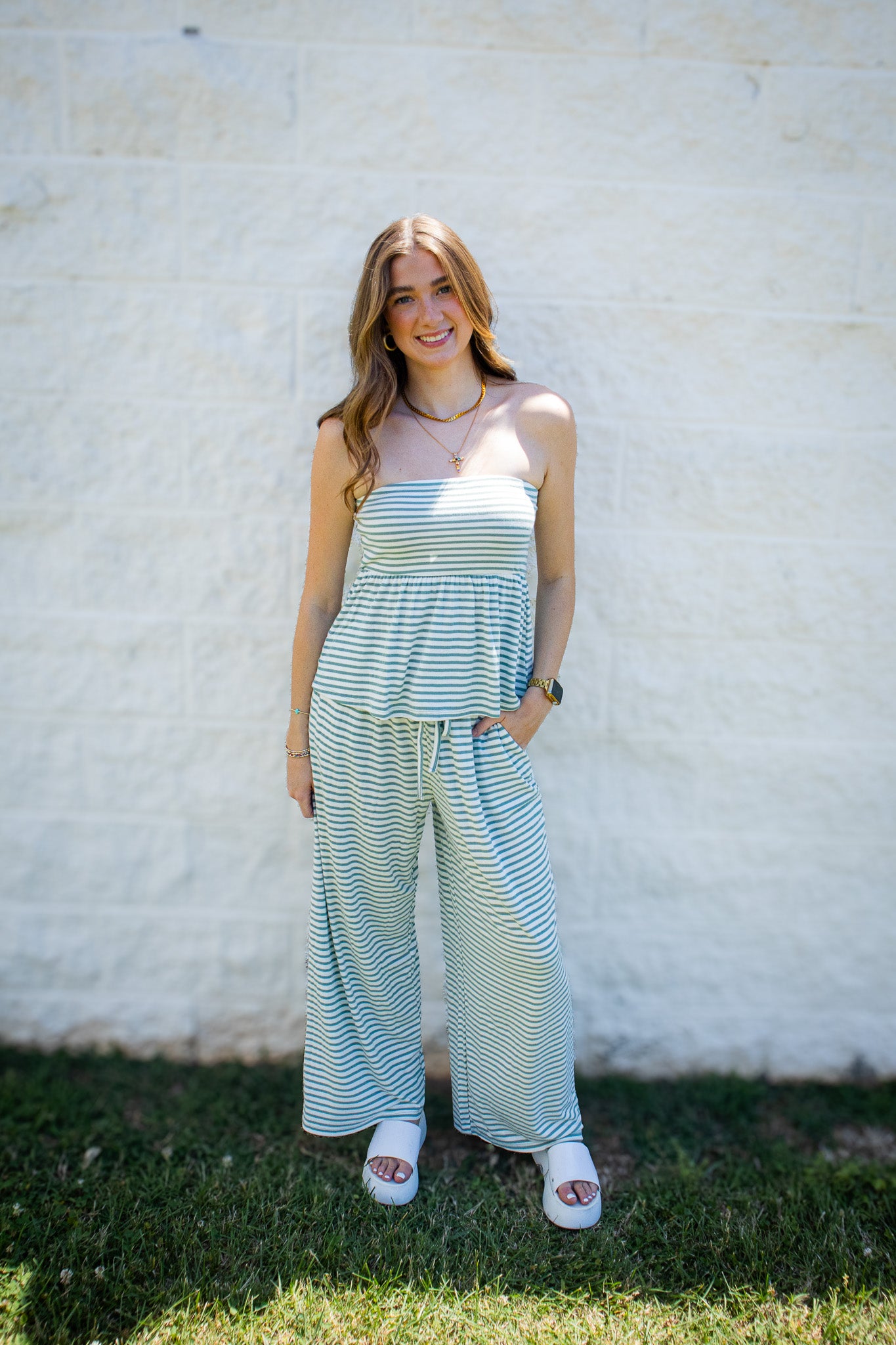 Model wearing a sage green and ivory striped strapless two-piece set with a peplum tube top and matching wide-leg drawstring pants, styled for summer boutique fashion.