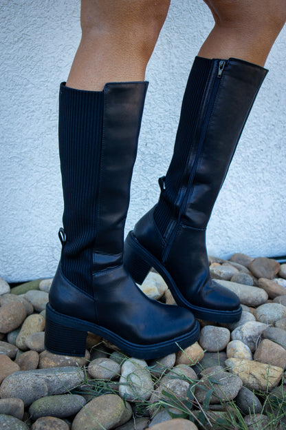 Black knee-high boots featuring a smooth faux leather finish, ribbed stretch back panel, inside zipper closure, chunky block heel, and platform sole for a sleek, comfortable fall look.