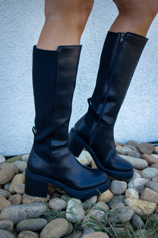 Black knee-high boots featuring a smooth faux leather finish, ribbed stretch back panel, inside zipper closure, chunky block heel, and platform sole for a sleek, comfortable fall look.
