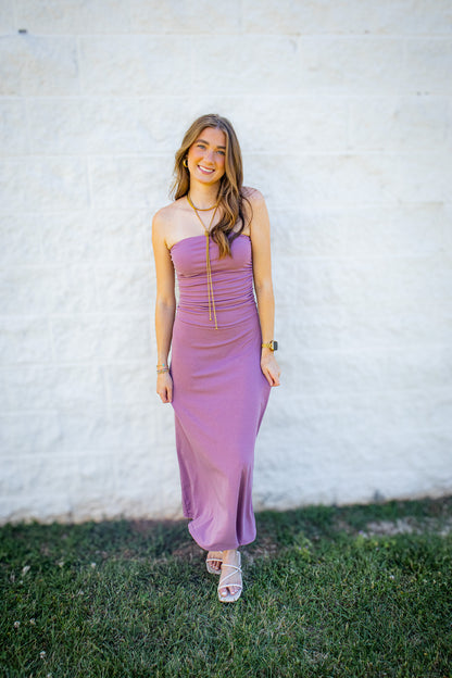 Women’s mauve strapless midi dress with ruched bodice styled with white heels and gold jewelry for a summer event outfit.