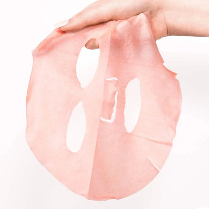 Pink face mask sheet held by a hand on a white background