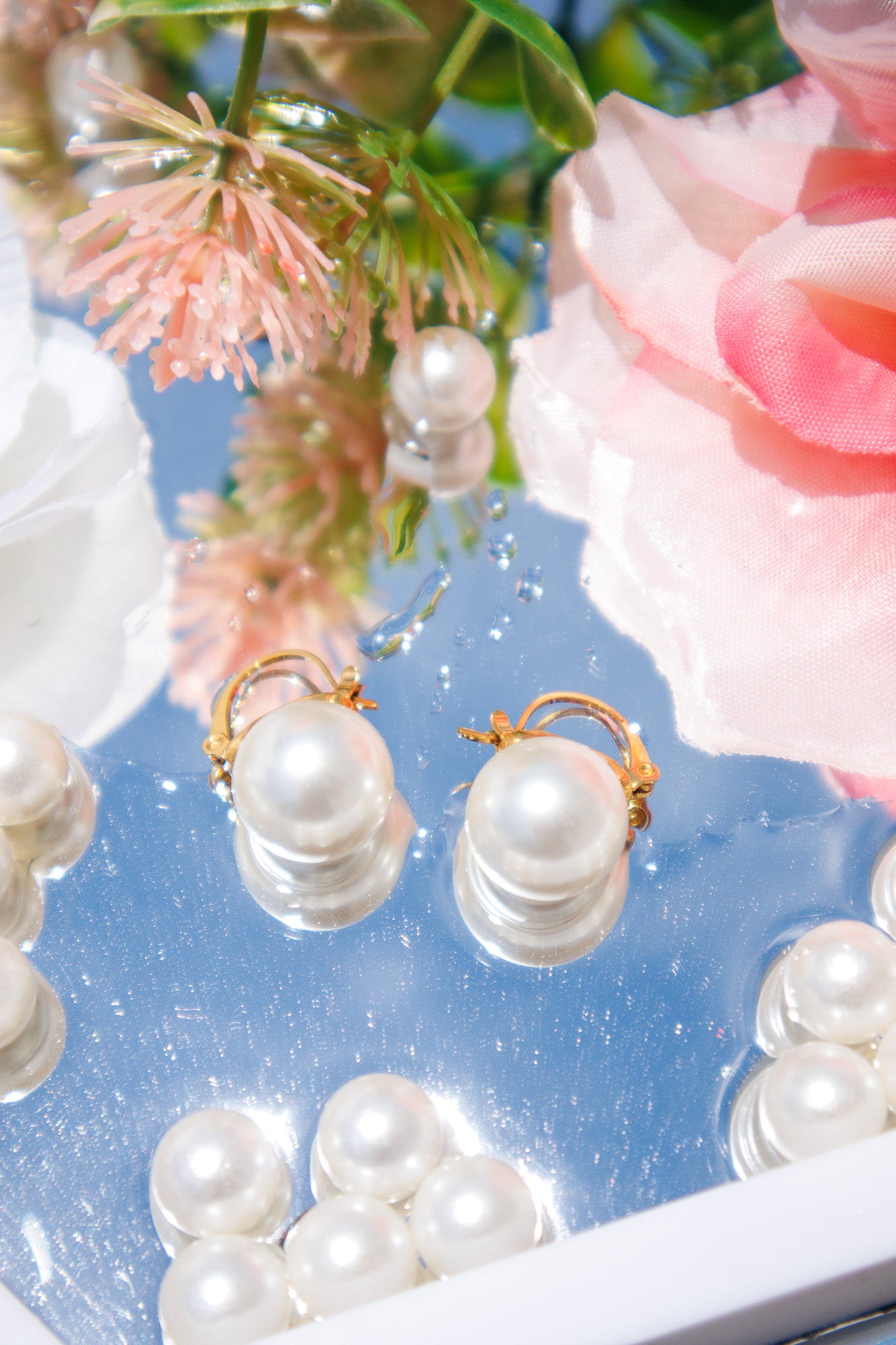 Pearl earrings displayed on a blue surface with flowers in the background