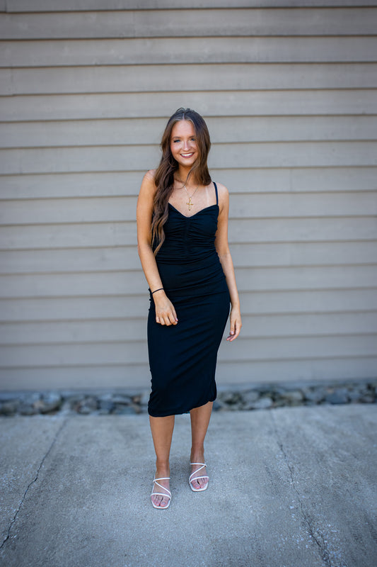 Black fitted midi dress outfit with ruched front, styled with gold cross necklace and neutral strappy sandals