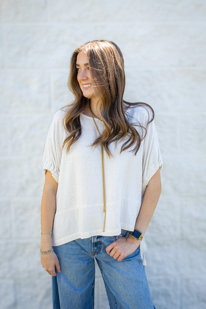 Women’s cream linen blend short sleeve top with gathered sleeves styled with light wash denim and gold jewelry.