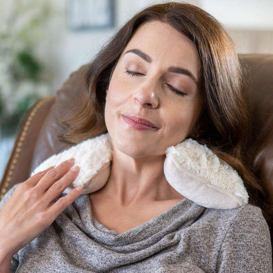 Woman relaxing in a chair with a plush  Warmies® neck wrap draped around her shoulders, providing soothing heat therapy and cozy comfort for neck and shoulder relief.