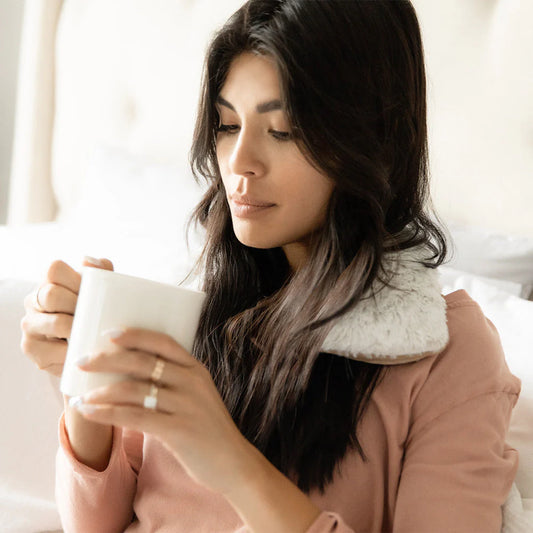 Woman relaxing with a plush  Warmies® neck wrap draped around her shoulders, providing soothing heat therapy and cozy comfort for neck and shoulder relief.