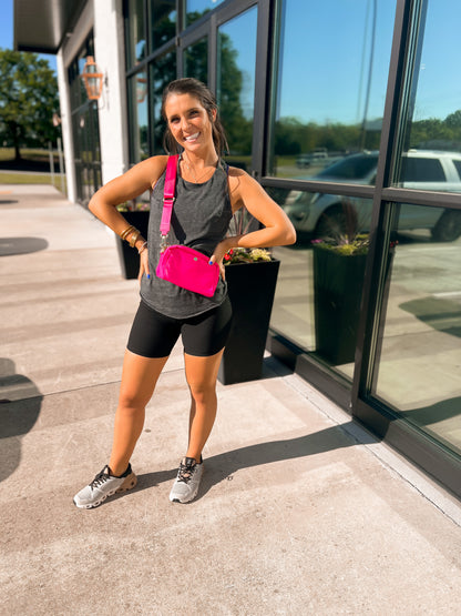 Woman in athletic wear with a pink bag standing outside a building.
